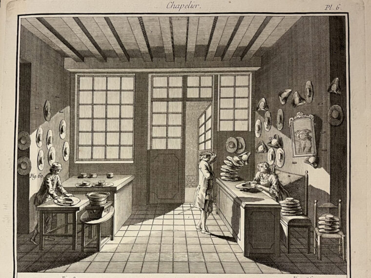 Gravure en noir et blanc représentant l’intérieur d’un atelier de chapelier au XVIIIe siècle. Un homme à gauche brosse un chapeau, un autre discute en client avec une femme derrière un comptoir. L’atelier est meublé de tables de travail, d’étagères garnies de moules à chapeaux, et éclairé par de grandes fenêtres à petits carreaux. Le sol est carrelé et le plafond à poutres apparentes.
